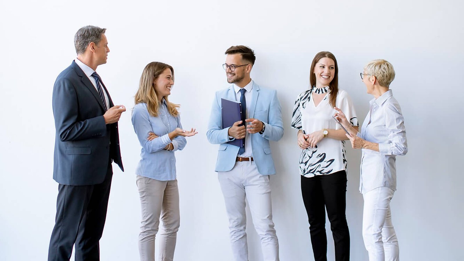 Five colleagues talking together against a white wall